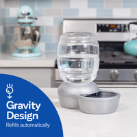 On the kitchen counter sits a Petmate Replendish Pet Waterer with Microban, featuring a clear jug and blue circle labeled Gravity Design Refills Automatically. It keeps pet water fresher while the tiled backsplash and appliances can be seen in the background.