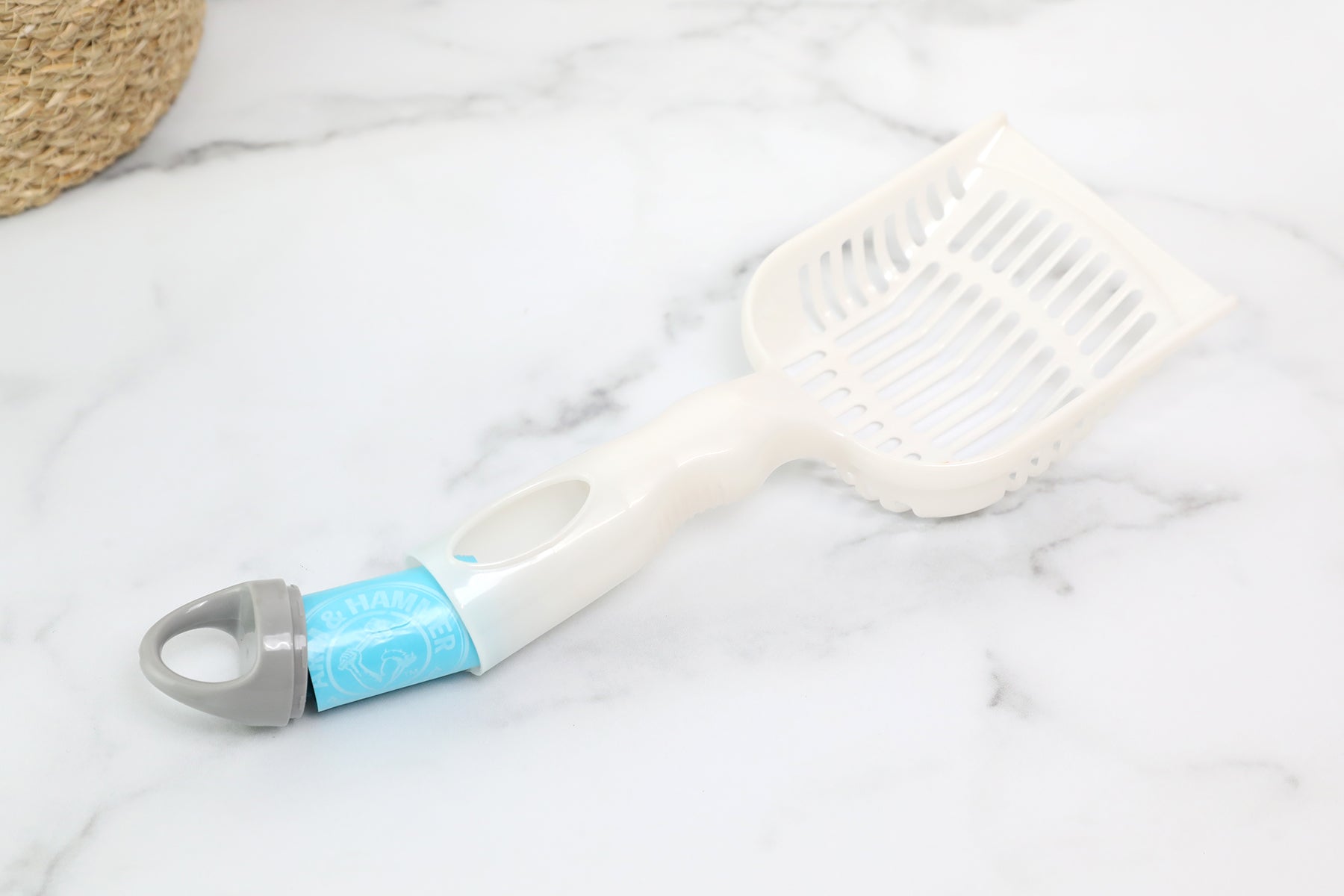 The Arm & Hammer Deluxe 2-In-1 Litter Scoop with Waste Bags, in white plastic with a gray handle and subtle blue label, is elegantly displayed on a marble surface.
