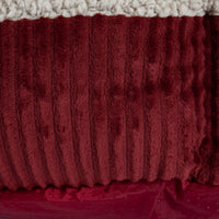 Close-up of the Aspen Pet Self-Warming Oval Lounger Pet Bed by Aspen Pet, featuring deep red, ribbed fleece fabric. The top layer is a soft cream material similar to faux lambs wool plush, while the bottom has a smooth red dotted surface for non-skid effect. It appears cozy and warm.