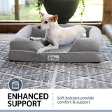 A small dog rests on a PetFusion Ultimate Dog Bed with gray memory foam and raised bolsters for joint pain relief. Set outdoors on a porch with plants, a label states: Enhanced Support: Soft bolsters provide comfort & support.