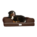A large black, brown, and white dog relaxes on a PetFusion Ultimate Dog Bed With Memory Foam in brown. The bed has raised cushioned edges for joint pain relief. The relaxed dog lies on its side with its mouth slightly open, while a small label with the Petfusion logo is visible on the bed.