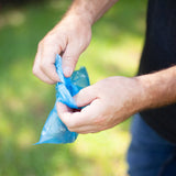 Hands holding an Arm & Hammer Easy-Tie Dog Waste Bag outdoors against a grassy background.