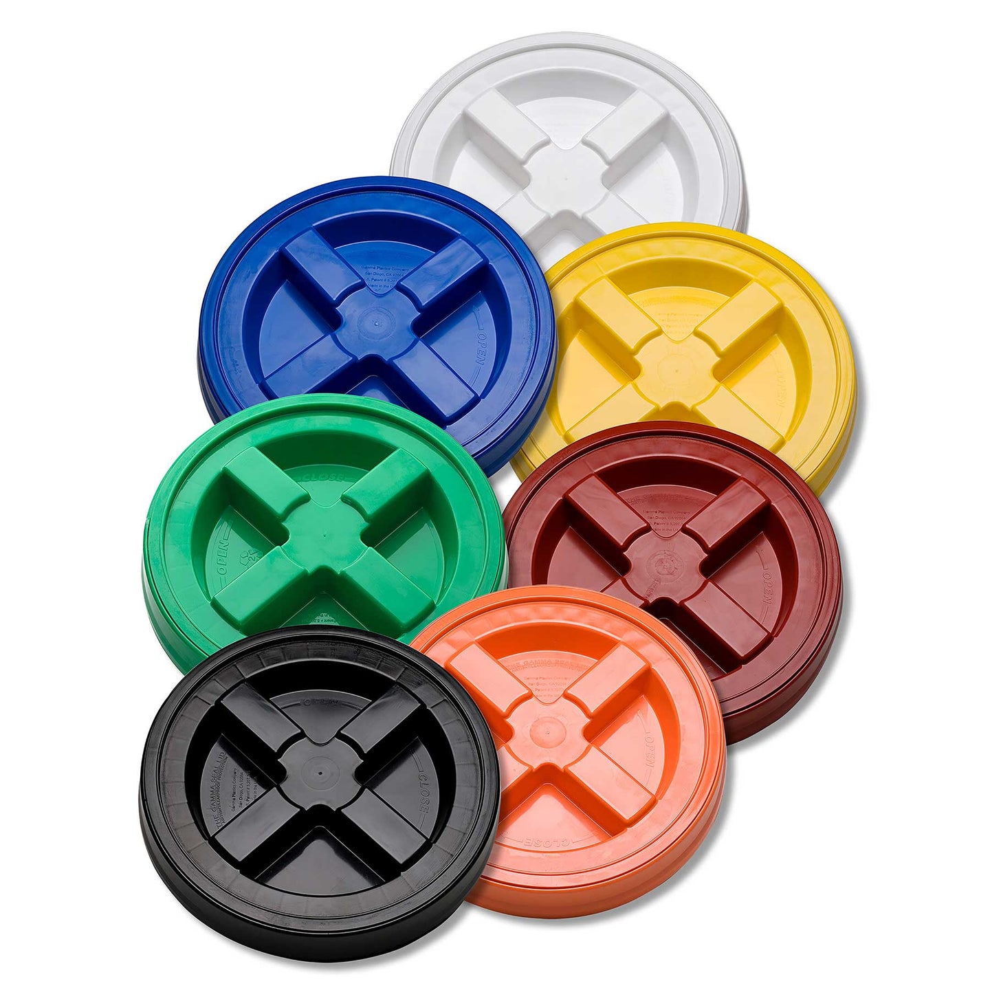 Seven GAMMA Seal Lids by Gamma2, made from BPA-free HDPE plastic, are displayed in a curved line. Available in white, yellow, blue, green, orange, red, and black hues, each features a cross-shaped center indentation for an airtight seal.