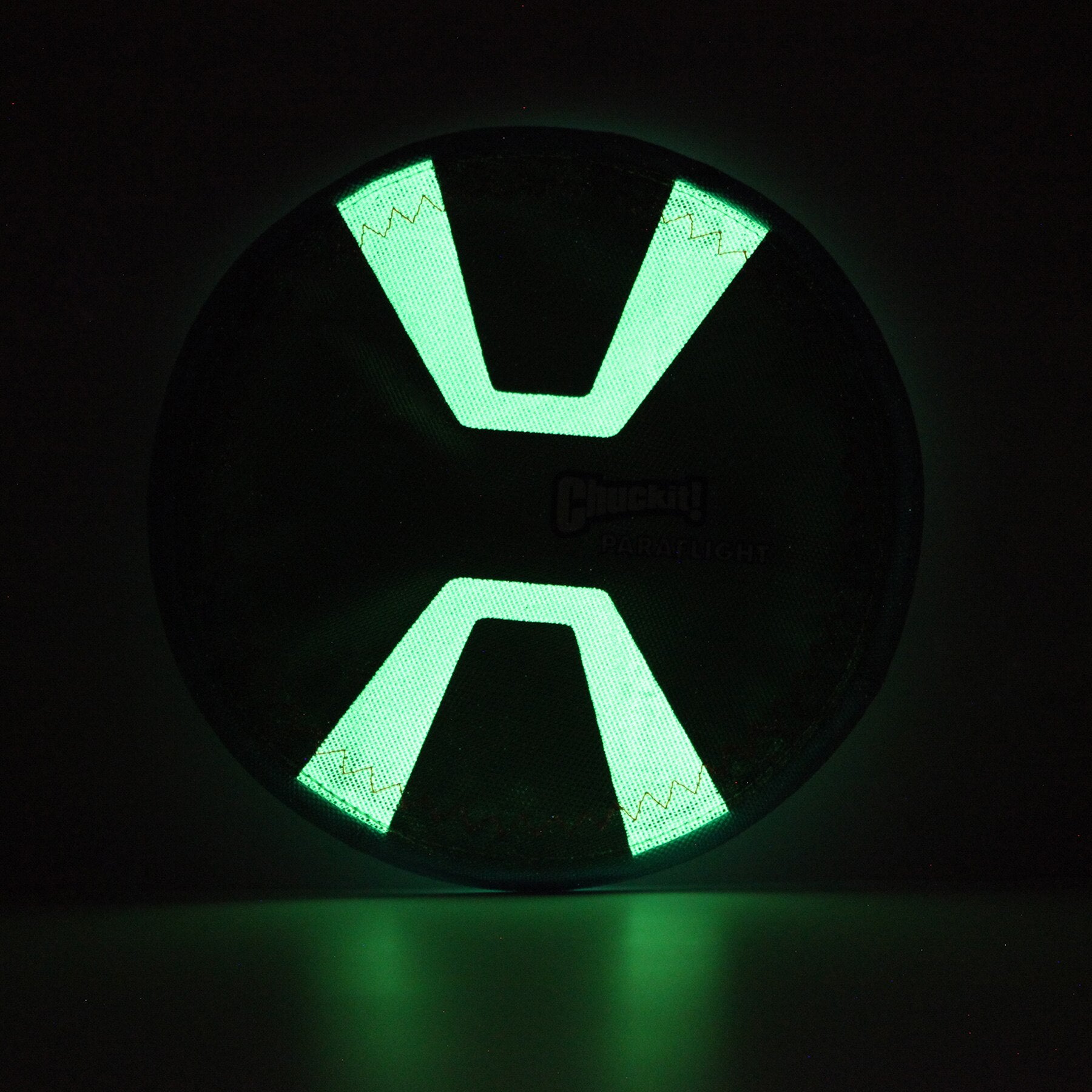 The Chuckit! Paraflight Max Glow Flyer Dog Toy is a glowing green and black circular accessory with an X-shaped center, emitting vivid light against the dark—a perfect choice for exciting nights of play.