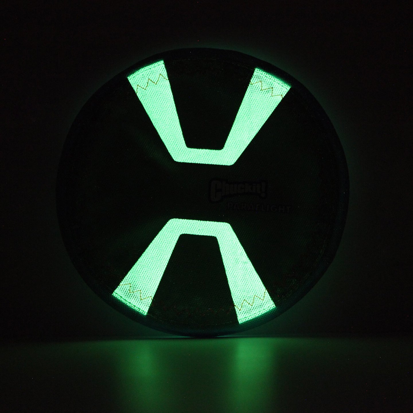The Chuckit! Paraflight Max Glow Flyer Dog Toy is a glowing green and black circular accessory with an X-shaped center, emitting vivid light against the dark—a perfect choice for exciting nights of play.