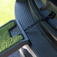Close-up of a cars trunk with the Gen7Pets Natural Step Ramp for Vehicles by Gen7, featuring a poly-grass surface. The ramp is secured with a black strap to the trunk interior, ready for use. Green grass stretches in the background, blending seamlessly with nature.