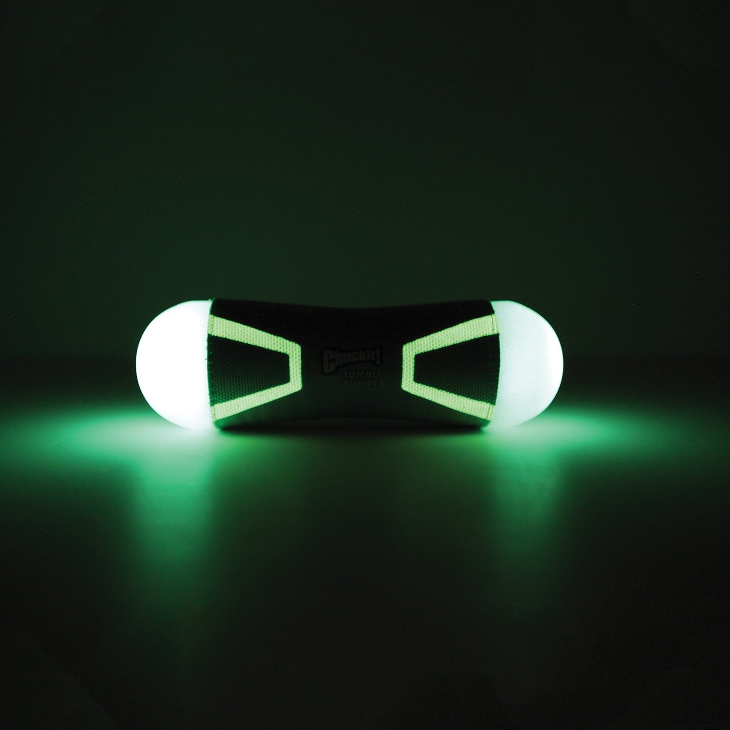 The Chuckit! Tumble Bumper Max Glow by Chuckit illuminates two ends with a black core in a dark environment. Its cylindrical shape and glowing green light resemble a futuristic fetch toy from another world.