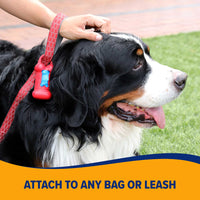 A large dog with a tricolor coat lies panting on grass, attached to a red leash featuring an Arm & Hammer Bone Dispenser & Disposable Waste Bag Set. A person gently pats the dogs head. Text reads, ATTACH TO ANY BAG OR LEASH.