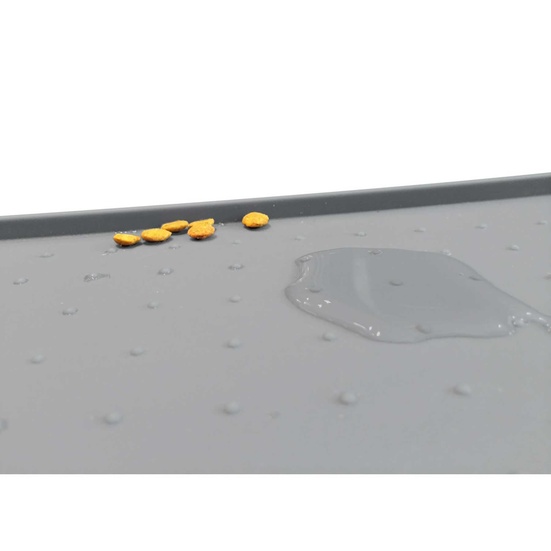 A gray PetFusion Pet Food Mat made from FDA-grade premium silicone with anti-slip bumps displays scattered yellow pills on the left and a puddle of clear liquid on the right.