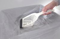 A hand sifts through a gray kitty litter box lined with a transparent plastic bag using the Aspen Pet No Tear Cat Litter Scoop, featuring a comfortable grip.
