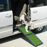 A small dog descends from a white minivan using the Gen7Pets Natural Step Ramp for Vehicles, featuring a poly-grass surface. The car door is open, and the scene is set under the sunny outdoors.